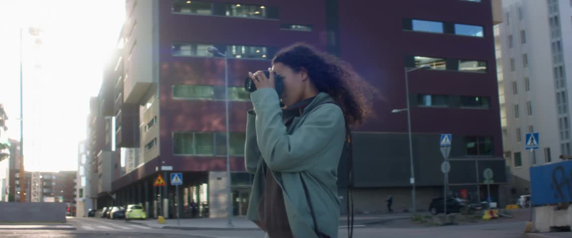 A woman stands outside near a city intersection and takes a photo with a professional camera