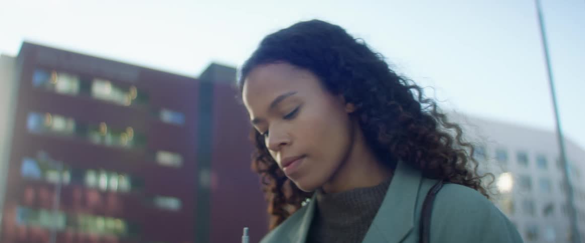 A young woman standing in downtown area looks at a pad of paper and writes on it
