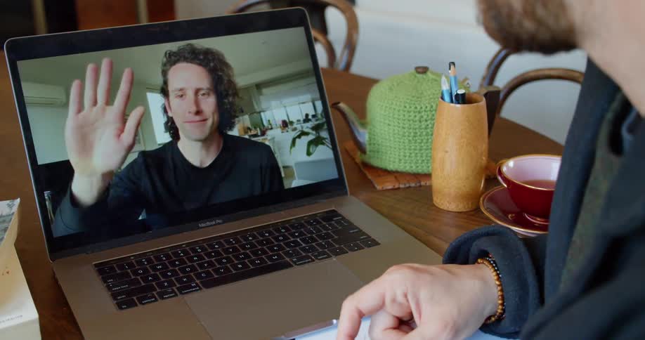 Two people wave goodbye on a laptop video call from home