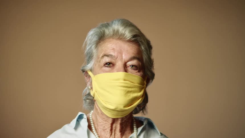 An elderly woman is wearing a yellow face mask and staring into the distance