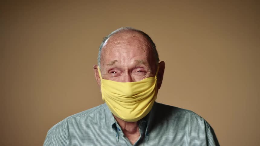An elderly man is wearing a yellow face mask