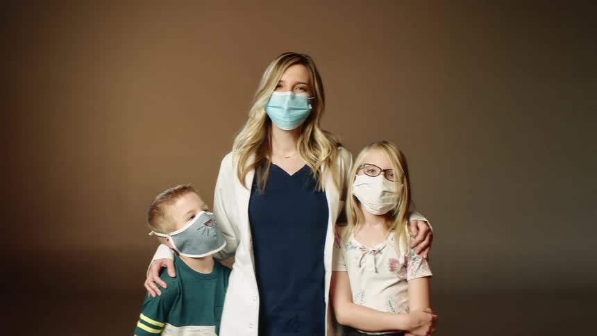 A woman a boy and a girl standing in a room wearing mask