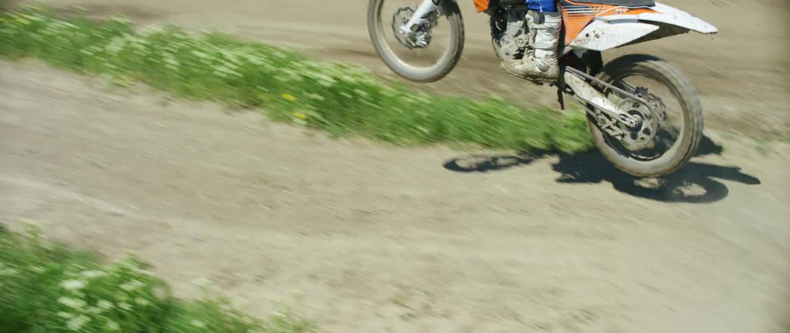 A male on a motocross bike jumps over a hill as he rides on a track
