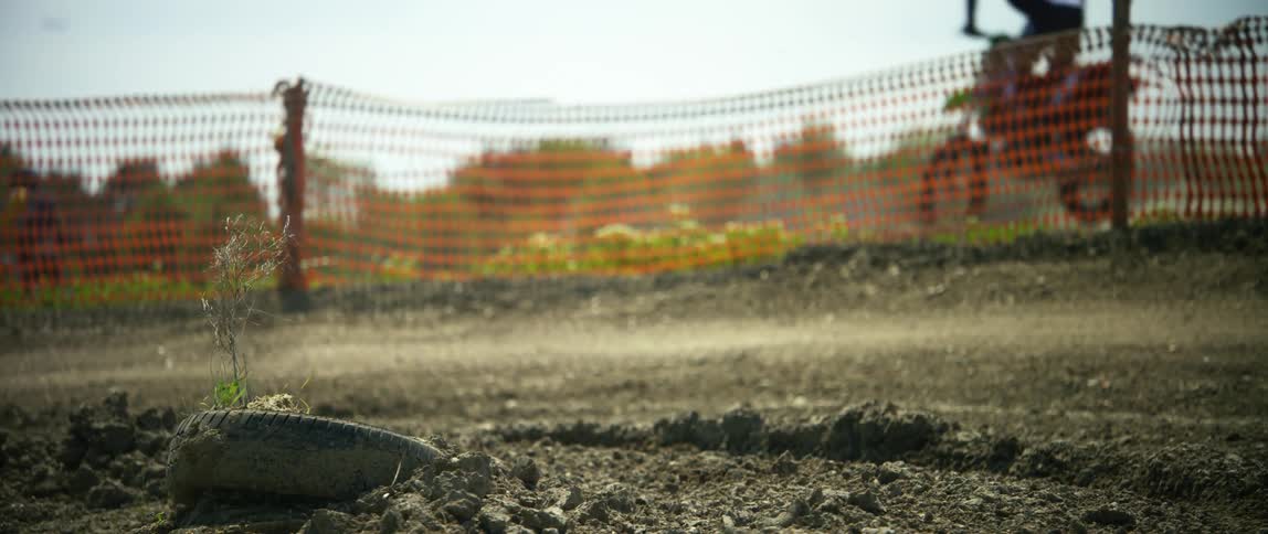 People with helmets riding dirt bikes on an obstacle course with the sky and clouds in the background