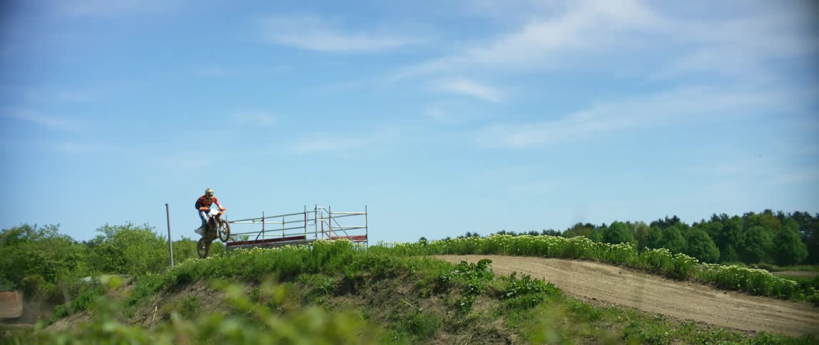 A motorbike rider jumps over a bridge on a dirt trail