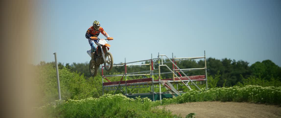 A motocross rider is sent airborne as they speed up a hill on a dirt motorcycle trail