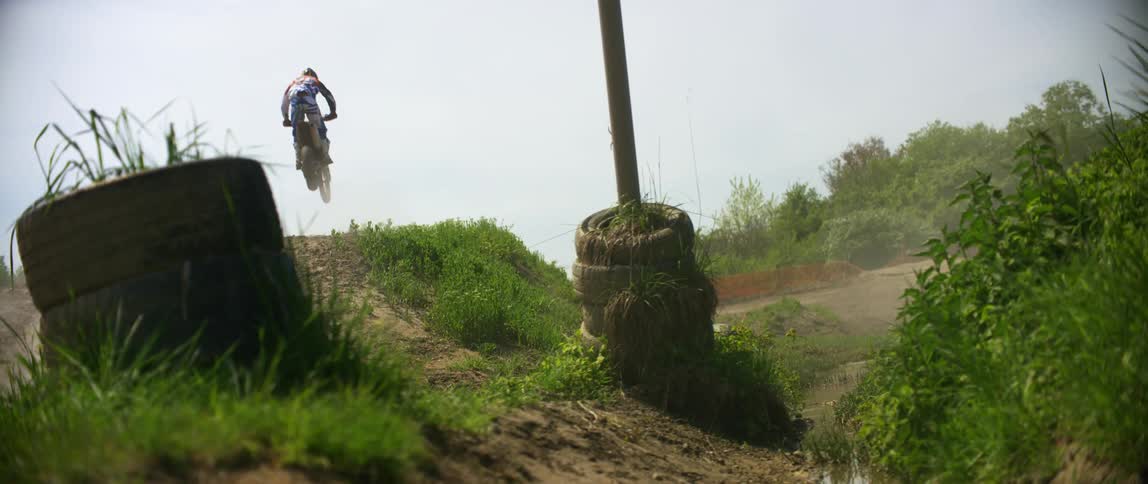 Man drives a dirt bike over a slope in a motocross track at day