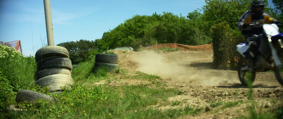 Person rides motorcycle along dirt course past stacked tires