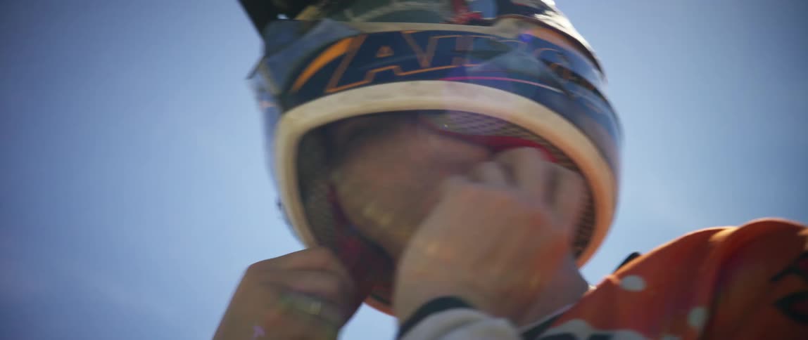 A motocross rider puts on and adjusts his helmet