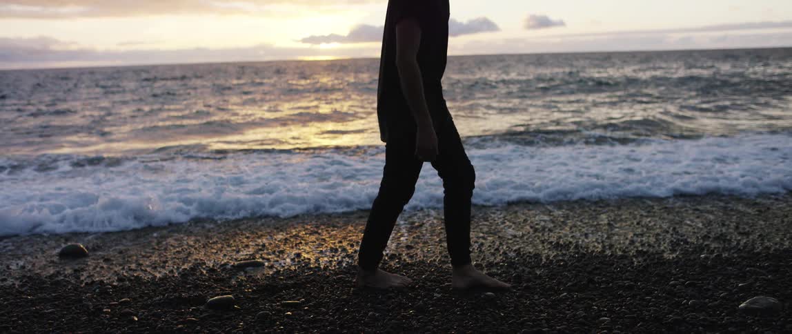A man is walking on the beach at dusk