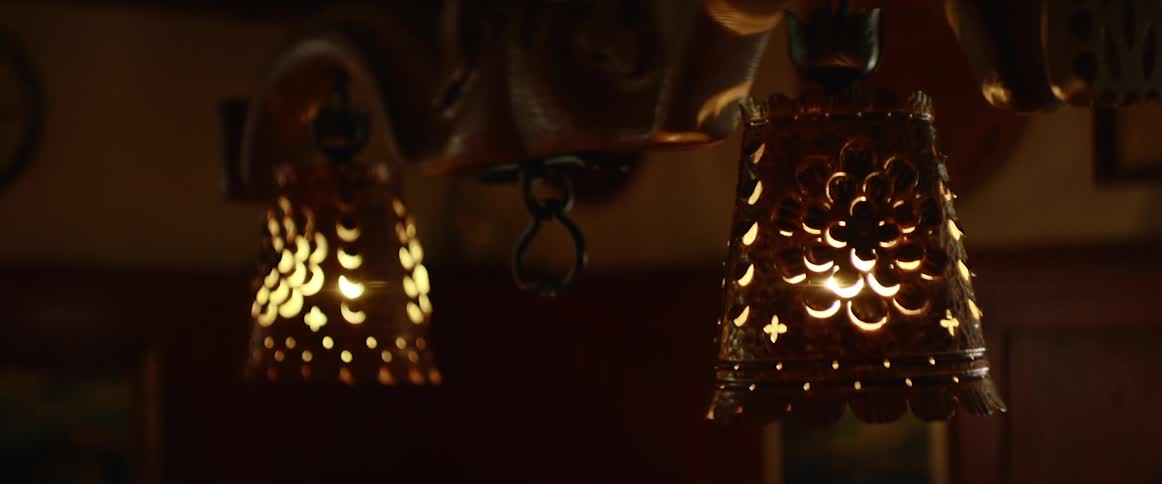 A chandelier with metal lamp shades hangs in a dimly lit room with artwork covering the wall