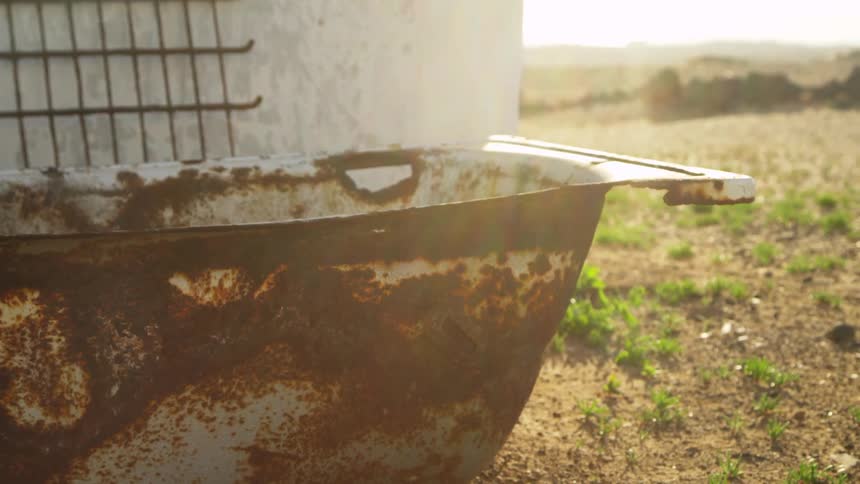 An old rusty bathtub next to a rural building on a sunny summer day