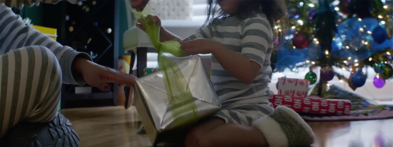 Little girl unwraps christmas present in front of a decorated christmas tree