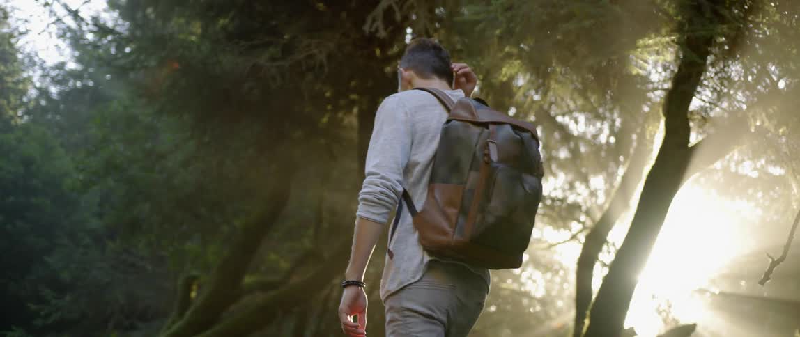 A man with a backpack walks under trees
