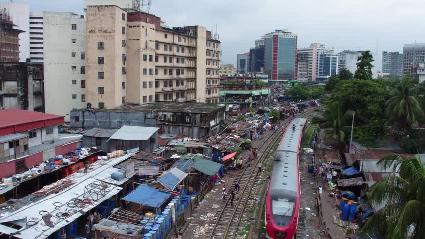 A train passes through a rundown section of a metropolis as people walk along the opposite track