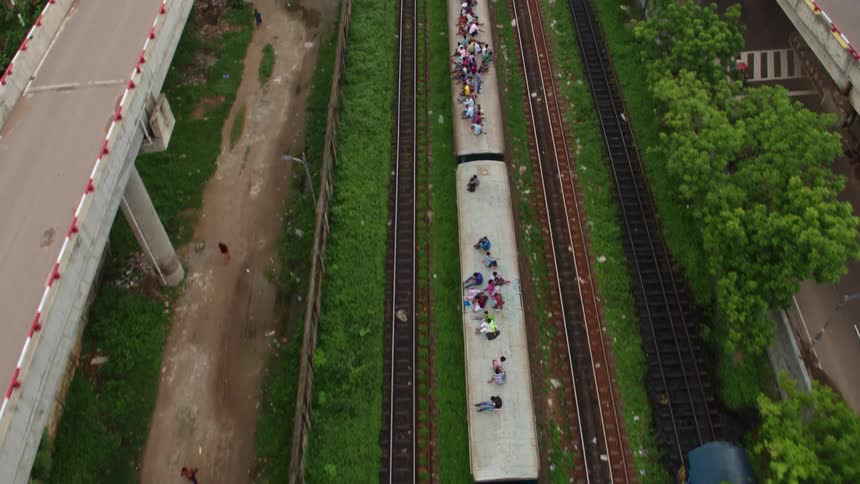 People ride on the rooftop of a train as it passes through a city during the day