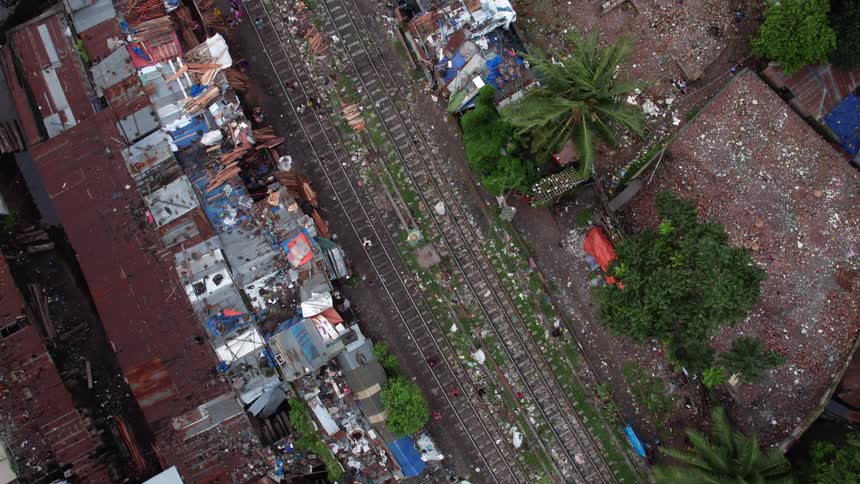 People walk along a pair of train tracks running through the slums of a city