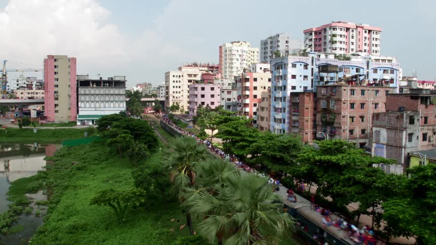 People ride on top of train cars passing through a city in a developing country