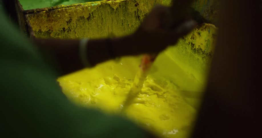 A boy uses a paddle to stir a balloon dye in a large tub