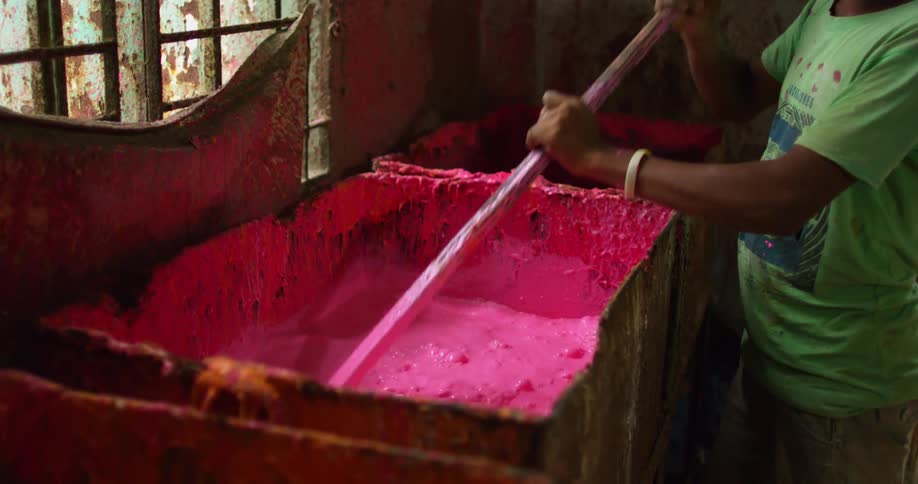 A teenage boy stirs a big container of pink dye