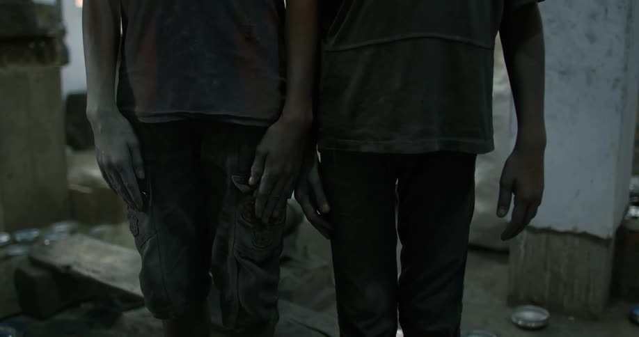 Two young boys with dirty hands and clothes stand next to each other in a building