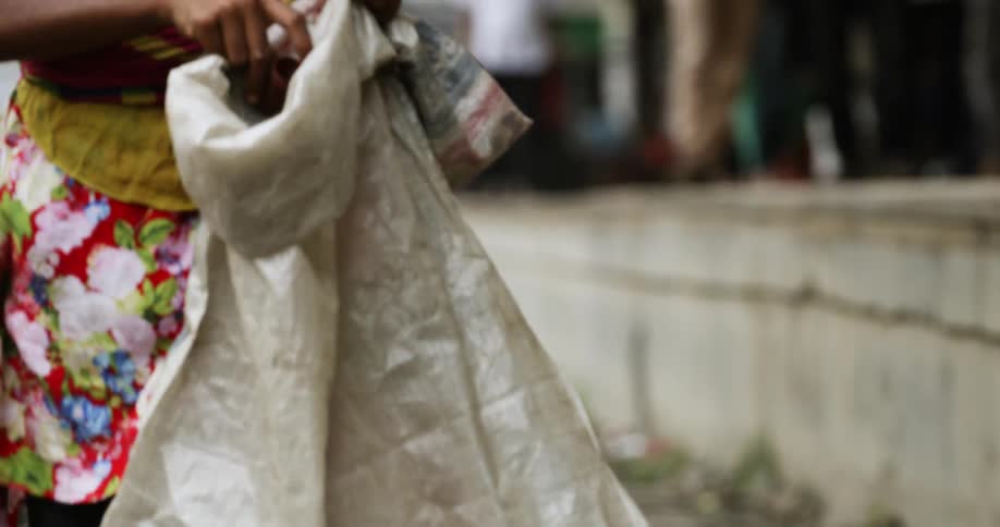 A girl walking down the street picking up litter and placing it in a bag