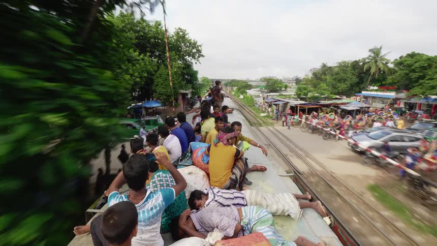 A train with children lying on top drives past outdoor shops in a primitive village