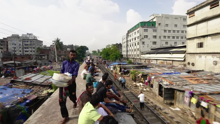 People sitting on top of a train with trees buildings and the sky in the background