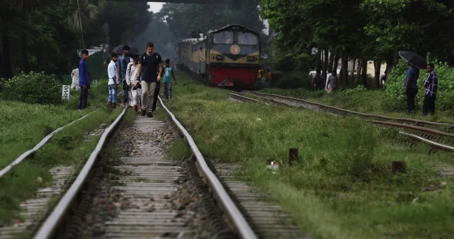 A group of people walk along a rural train track with a train on the track next to them