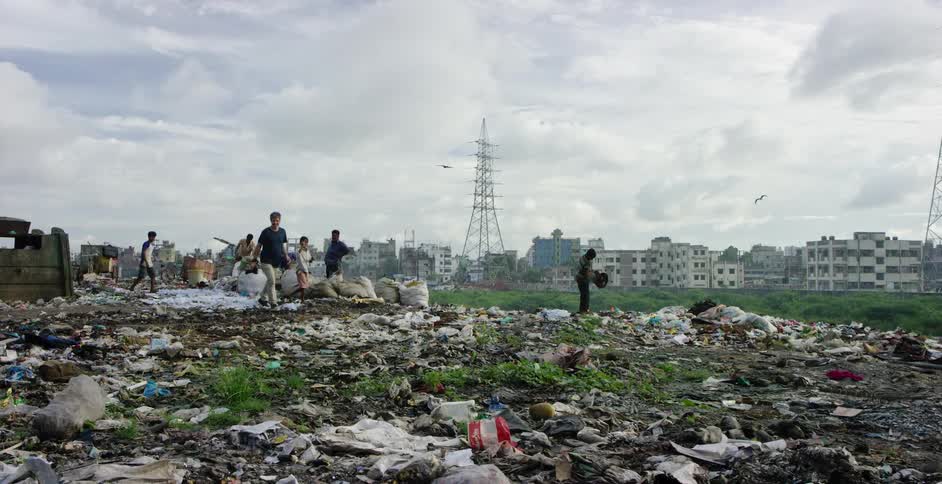 A photographer walks away from a group of children digging in a garbage pile on the outskirts of a third world city