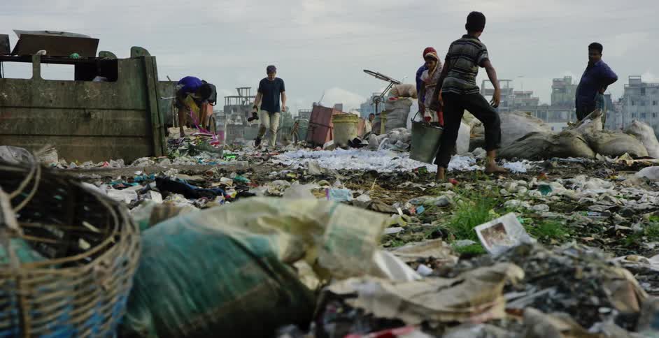 A photographer walks amidst people in a developing country as they pick through garbage