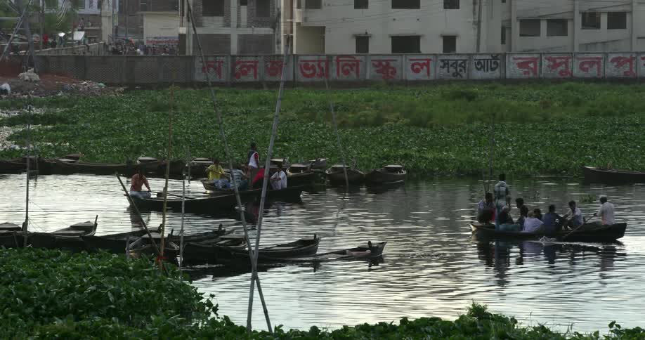 People ride rowboats along a river in a city during the day