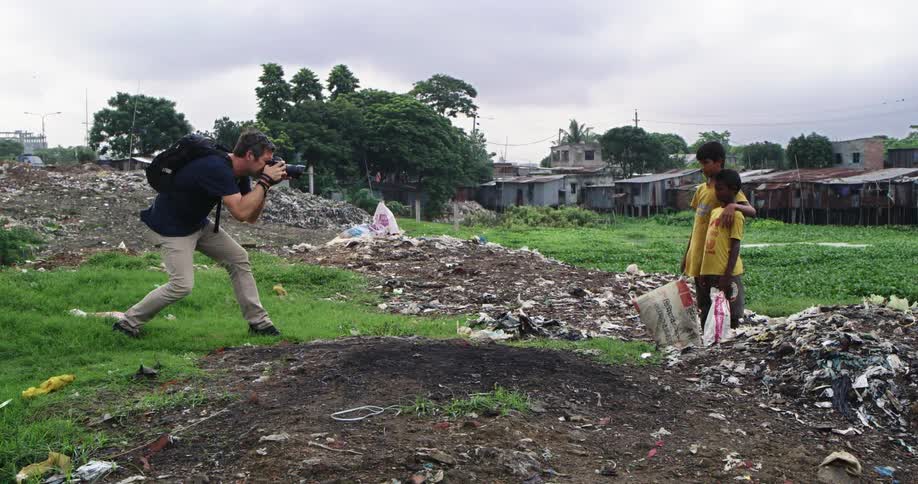 Photographer uses a camera to take pictures of two boys standing on a landfill near a slum