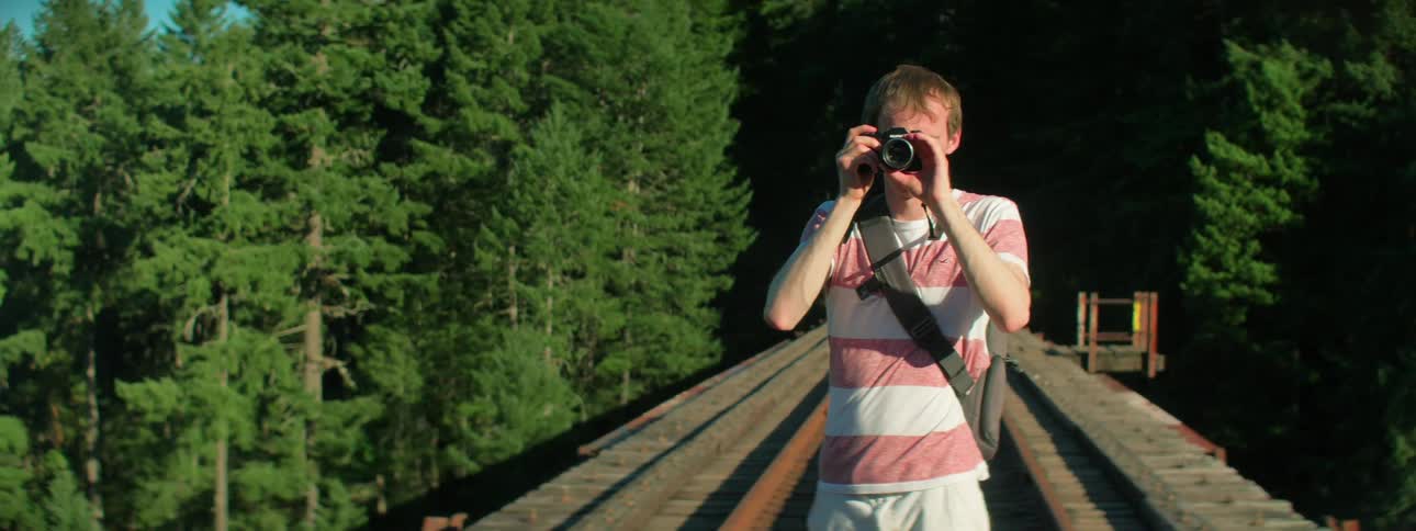 A man with a backpack and a camera standing on train tracks with trees in the background