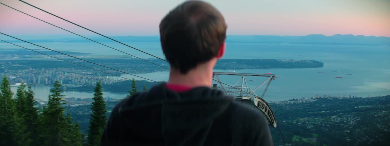 A man stands near the top of a ski lift and looks over the neighborhood and ocean below him