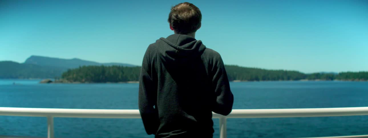 A boy standing against a railing looks out at the water