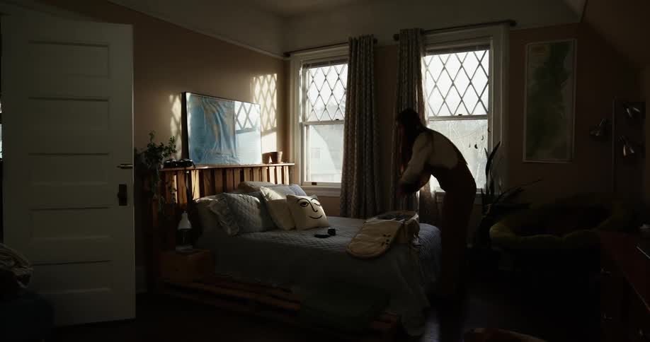 A woman picks up items from her bed and places them inside a small suitcase