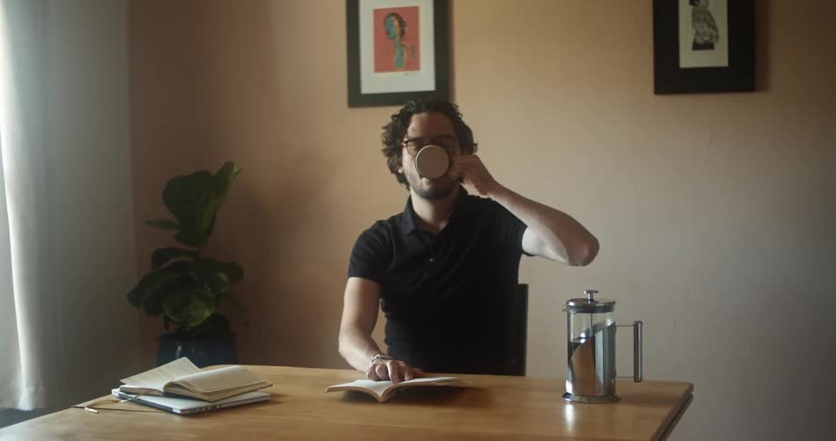 A man is drinking coffee and reading a book indoors
