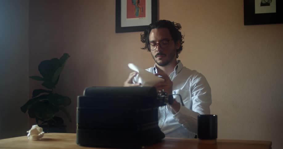 A man takes a piece of paper out of a typewriter and crumples it up