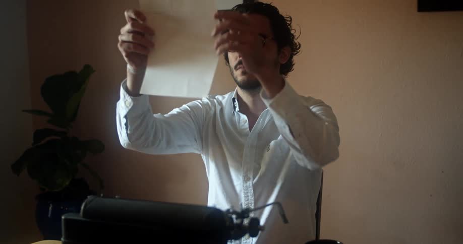 Young man in a white shirt and glasses pulls out a sheet of paper from a typewriter