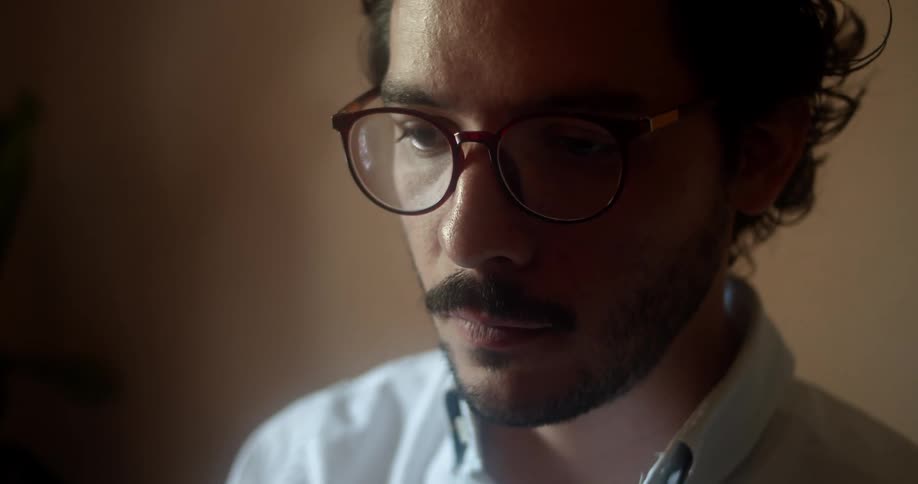 Man with glasses beard and a white shirt sits at a table and uses a laptop