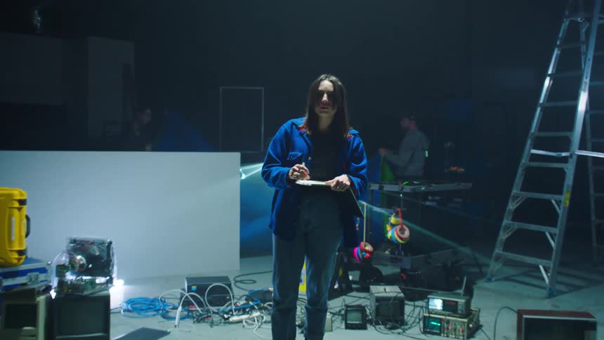 Two men work on a set as a woman checks off inventory