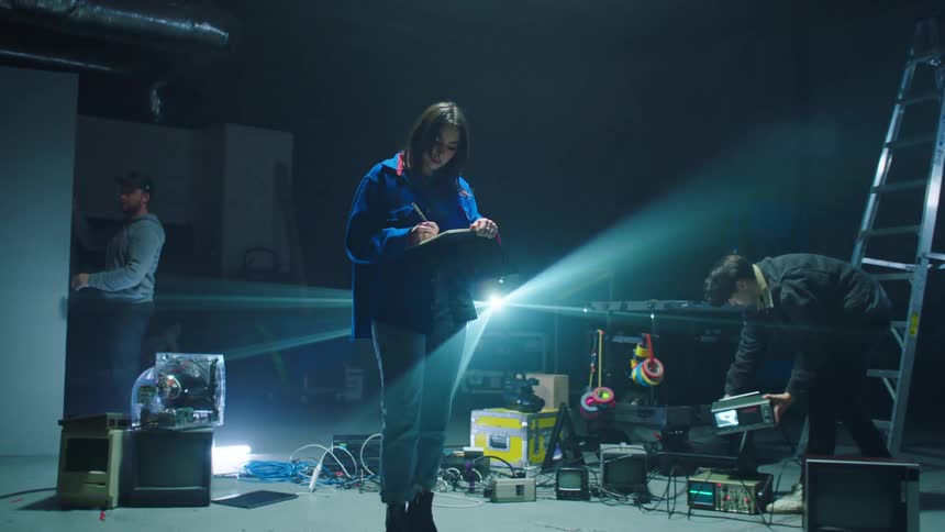 Two men and a woman backstage with equipment lights and a ladder