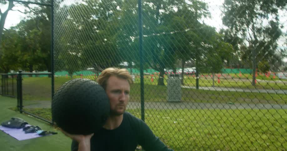Young man exercising in a park lifts a weighted ball with a single hand