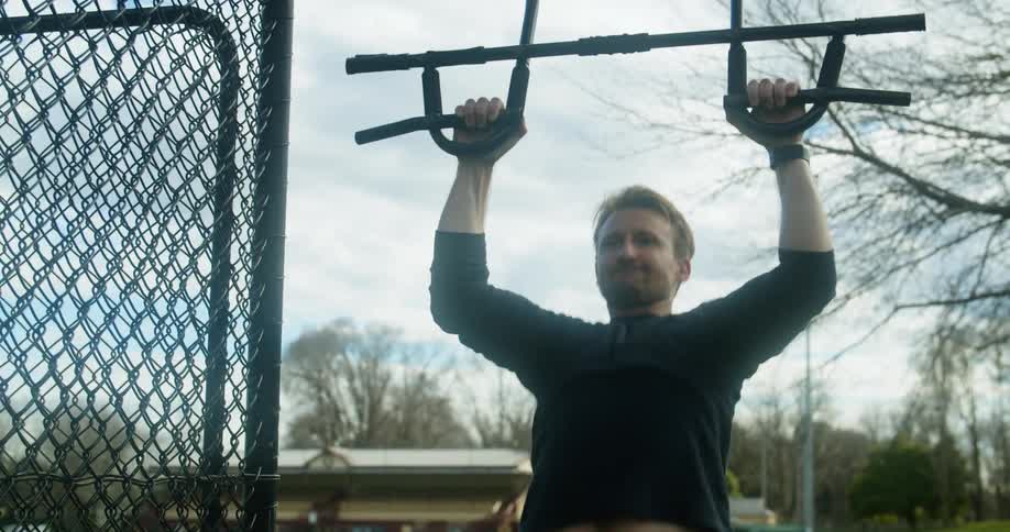 A young man does pull ups on outdoor exercising equipment during the day