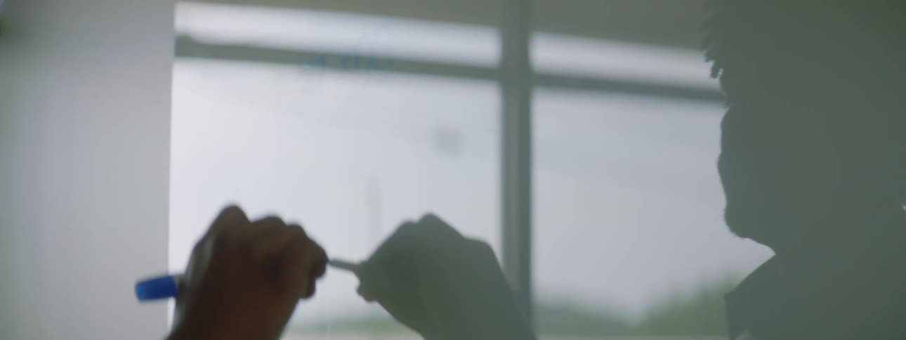 A man in an office writing on a white board