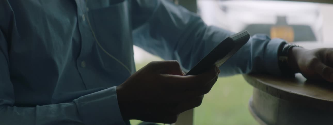 A man wearing earbuds uses his smartphone while sitting at a table indoors