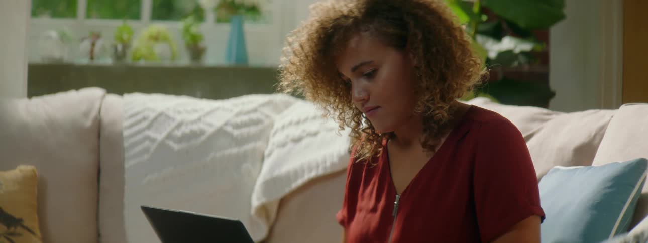 A young woman sits on a couch as she types on the keyboard of her laptop