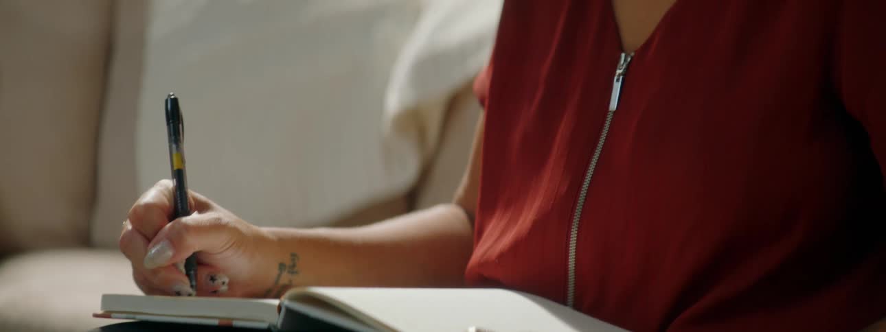 A woman sits on a couch writing in a book