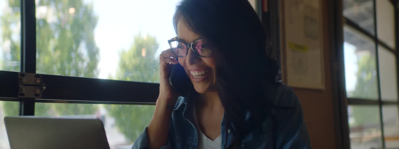 Young woman sitting at table with laptop answers phone call